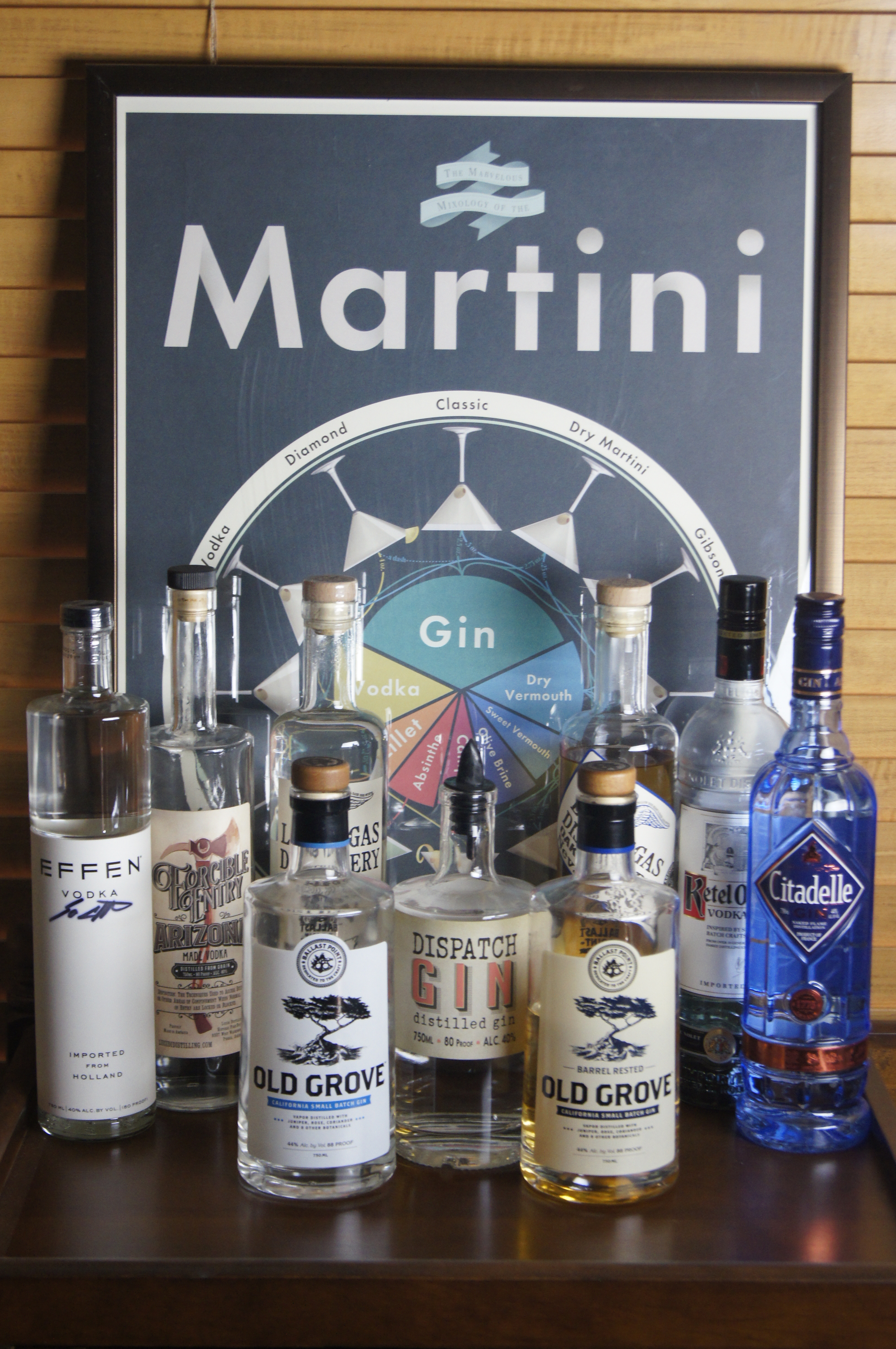 A martini poster behind a selection of 12 various vodka and gin bottles.  